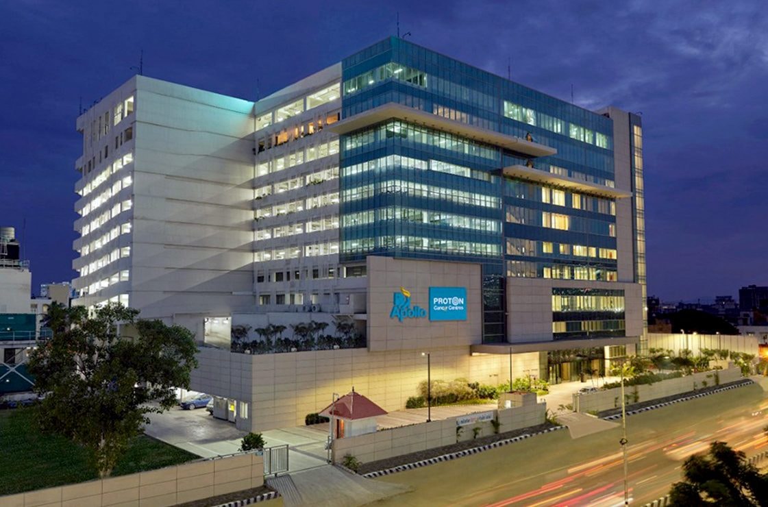 Apollo Proton Cancer Centre glass tower in Chennai lit up at dusk